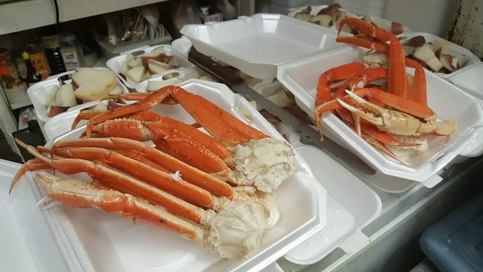 Two trays of cooked snow crab leg clusters on a counter, with cut potatoes beside them