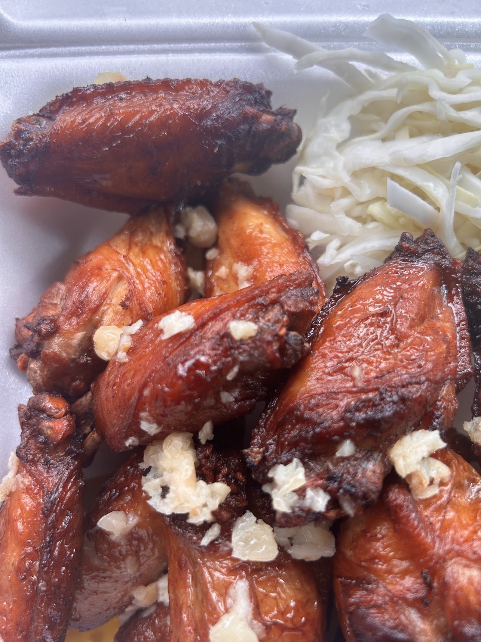 A close stack of fried chicken wings topped with chopped garlic, with shredded coleslaw to the side