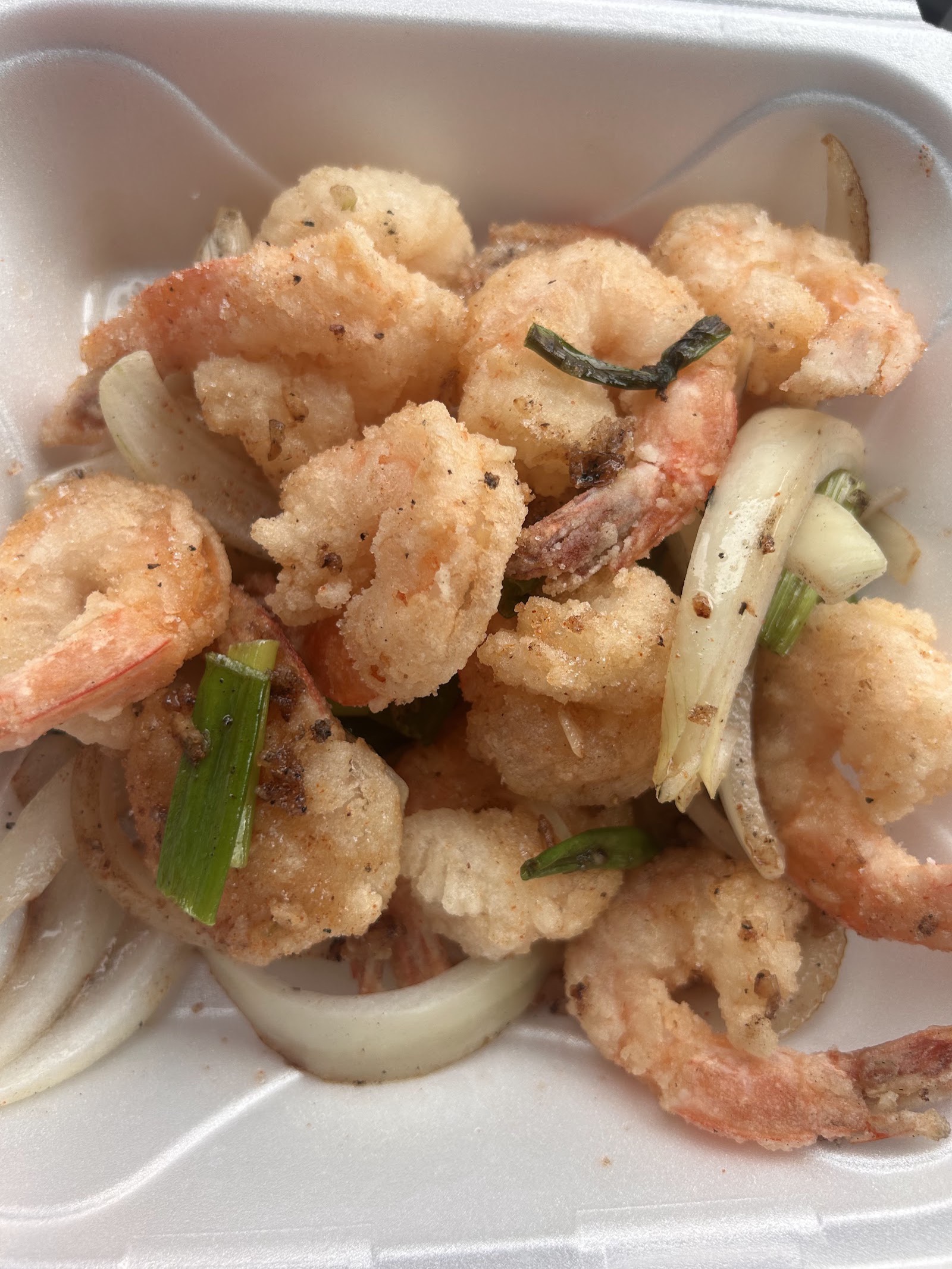 A takeout tray of fried shrimp with sliced onion and scallion